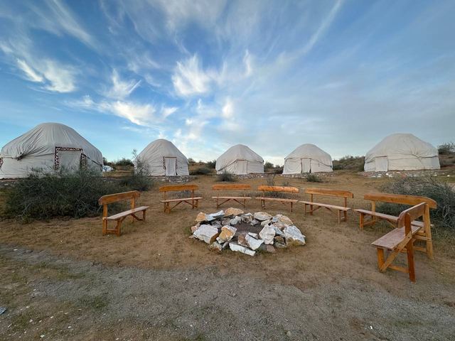 Yurts and a stone fire pit ringed with wooden benches under a wide desert sky